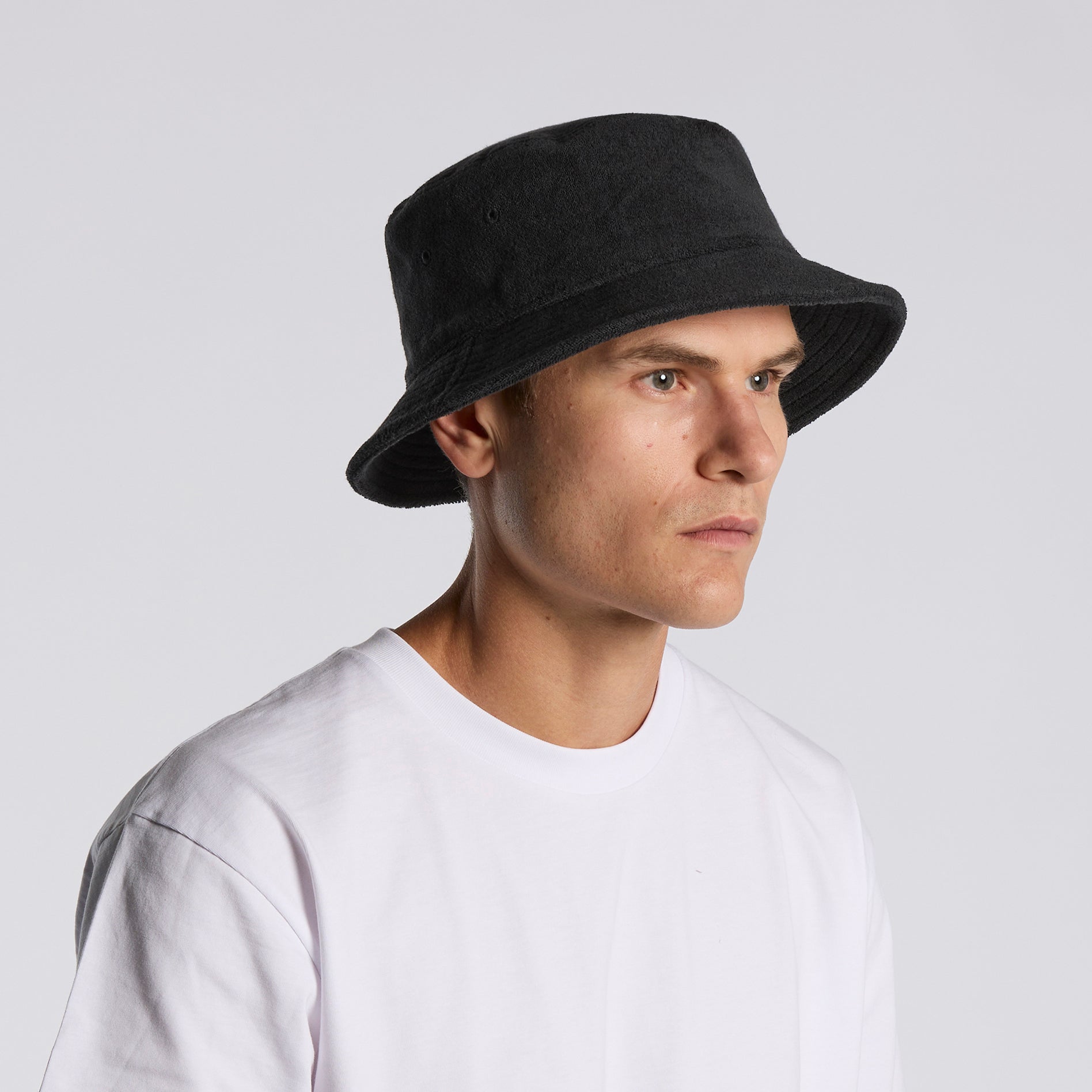 Man wearing a black as colour terry bucket hat side view against a plain background