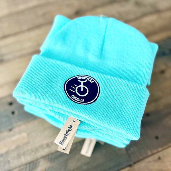 Turquoise beanie embroidered with a logo and brand tag on a wooden surface