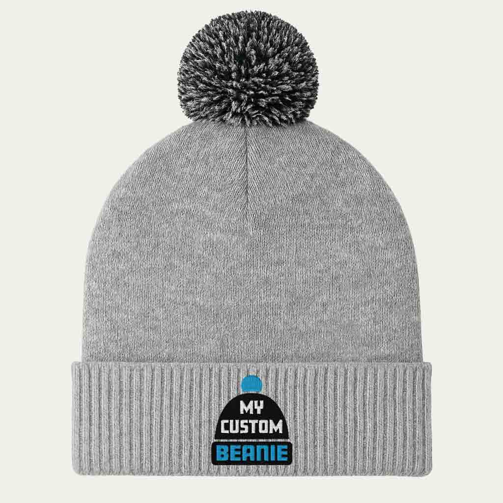 Grey beanie with pom-pom on a light grey background with embroidered my custom beanie logo