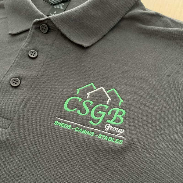 Gray polo shirt with green embroidered logo on a wooden surface