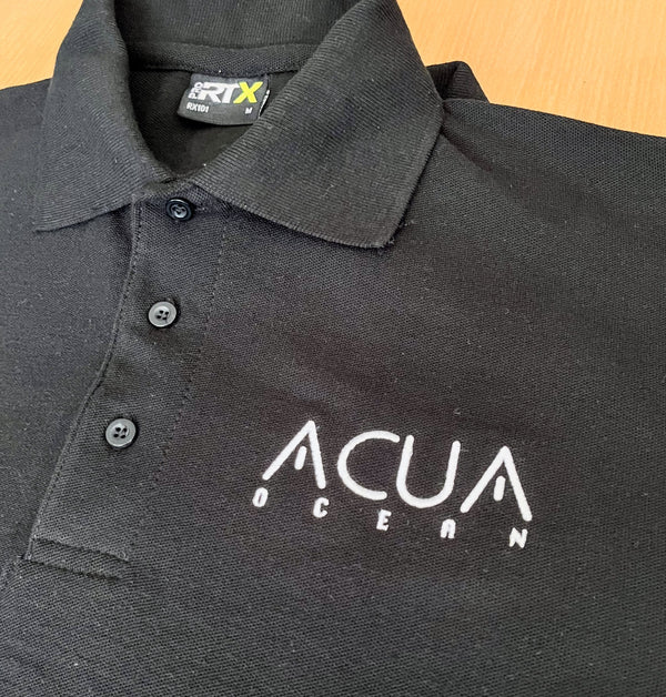 Black polo shirt with 'ACUA OCEAN' logo on a wooden surface