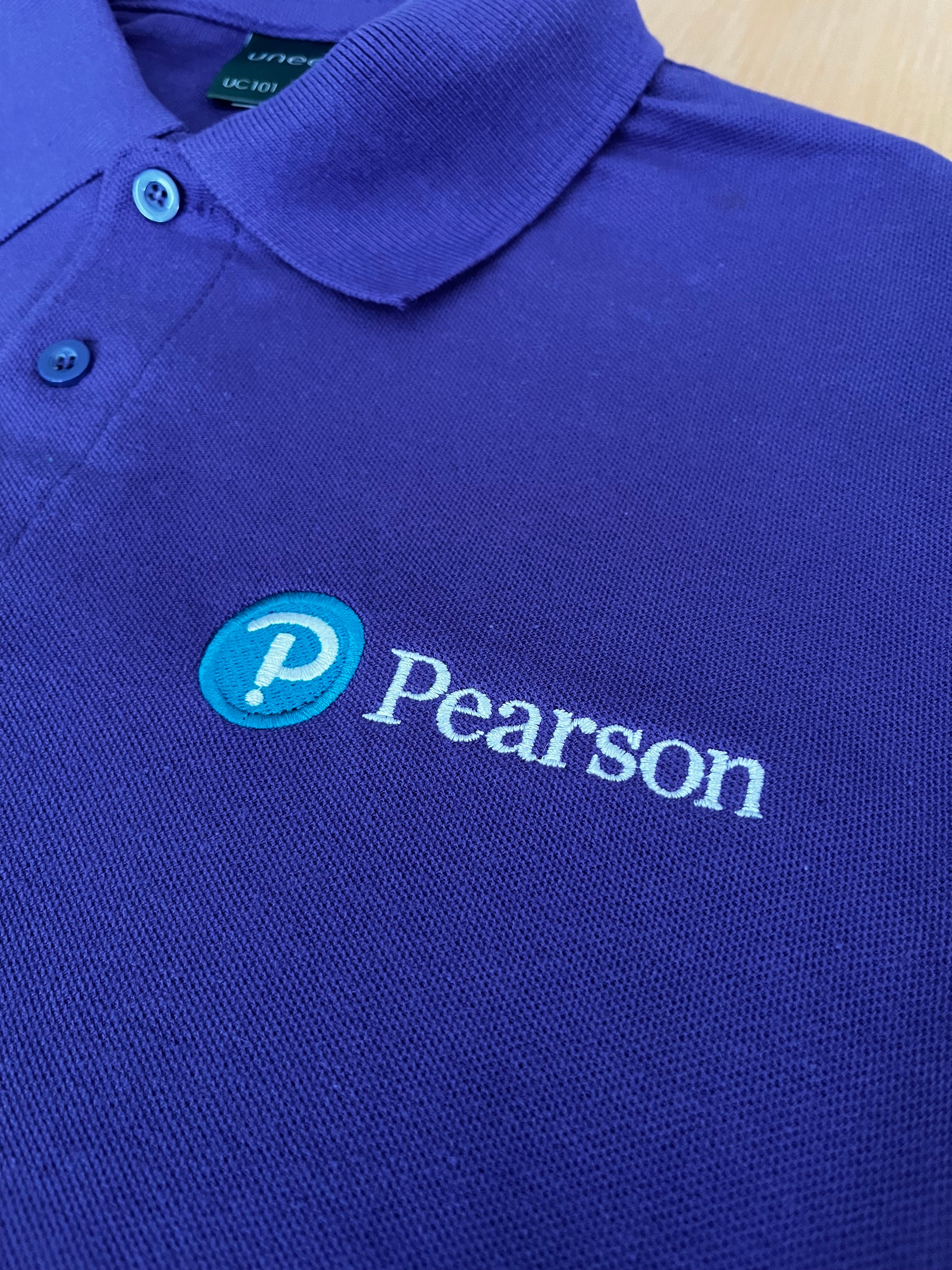 Blue polo shirt with Pearson logo on a wooden surface