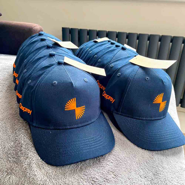 Blue baseball caps with orange embroidered logo on a grey surface
