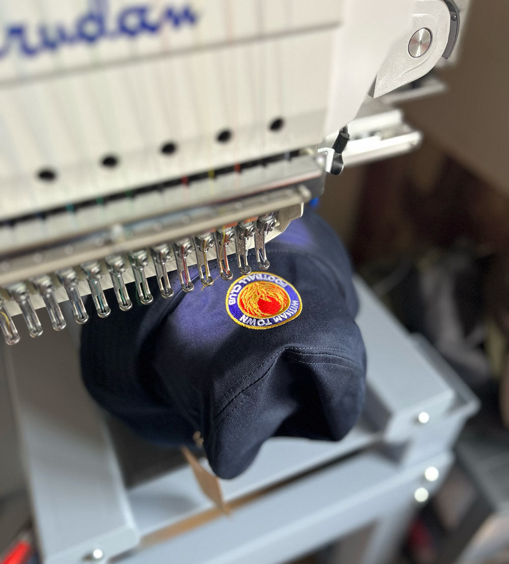 Embroidery machine with a navy blue cap being embroidered on a blurred background