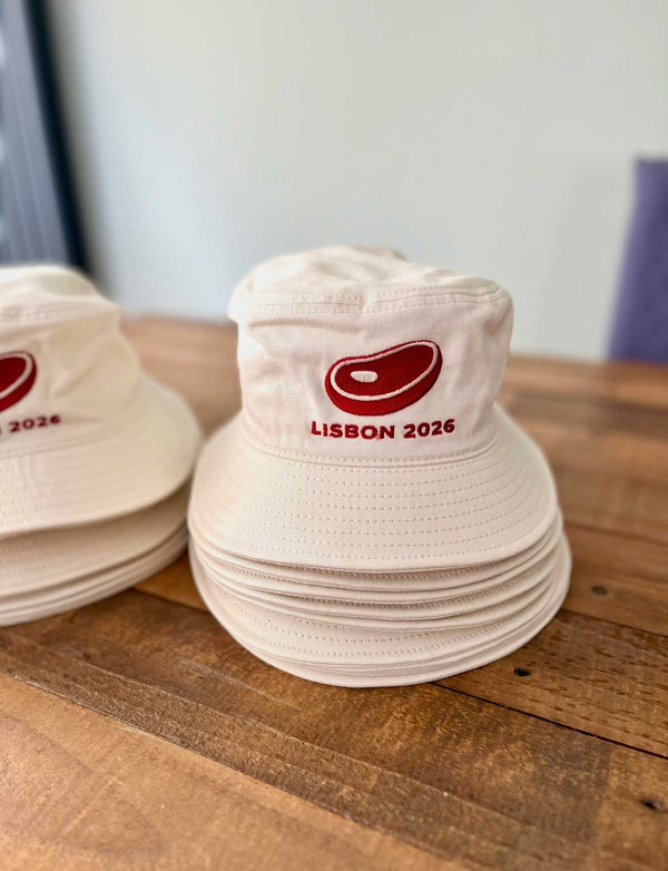 Stack of white bucket hats with 'Lisbon 2026' logo on a wooden surface