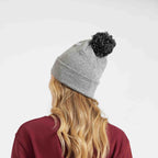 Person wearing a gray beanie with a black pom-pom on a white background