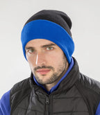 male model wearing Result Recycled Compass Beanie in colour black and royal blue photographed on a grey backrground