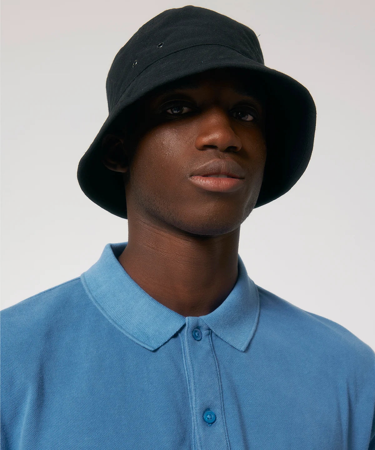 Man wearing black stanley stella bucket hat with metal eyelets on a white background