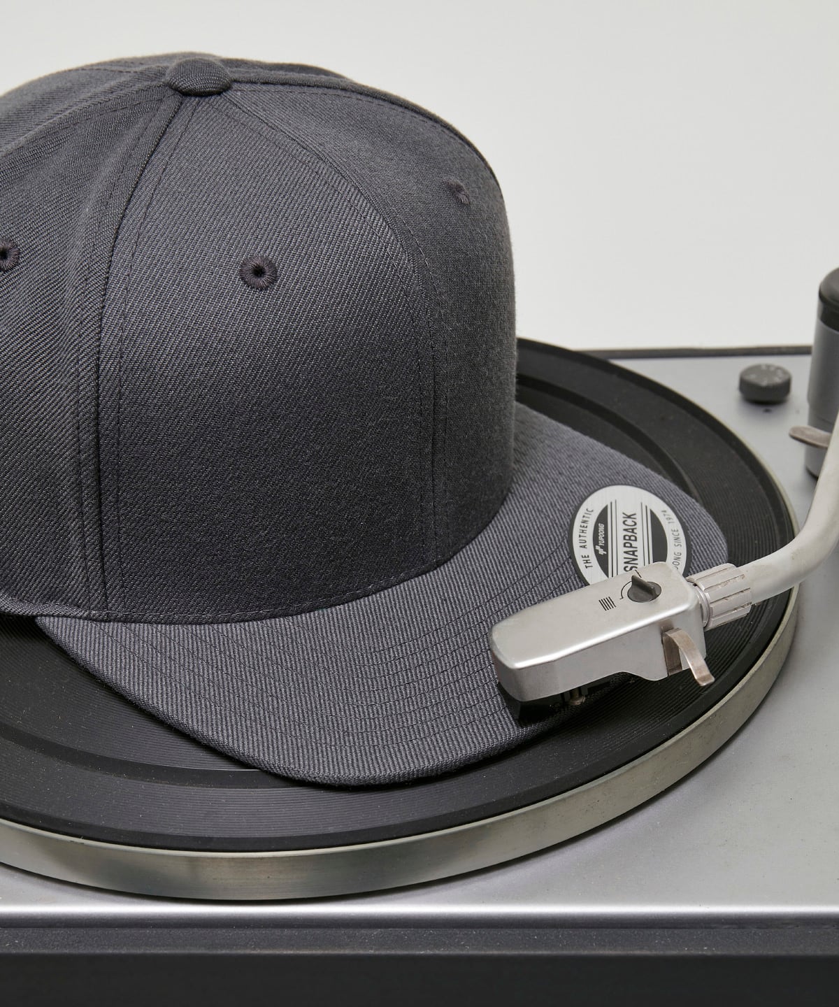 product image of flexfit classic snapback baseball cap in the colour dark grey viewed from the side photographed on a record turntable